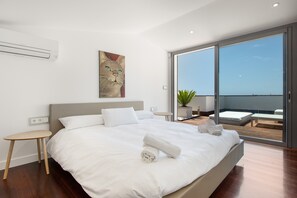 Een moderne hotelkamer met een groot bed, een klein nachtkastje, een schilderij aan de muur en een balkon met uitzicht.