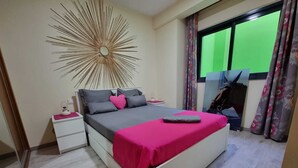 A bedroom with a bed, nightstand, mirror, and a large sunburst wall decoration.