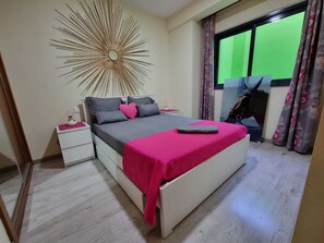 Une chambre à coucher comprenant un lit, une table de chevet, un miroir et une grande décoration murale en forme de soleil rayonnant.