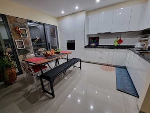 Een moderne keuken met witte kastjes, een zwart aanrechtblad en een eethoek met een bank en tafel.