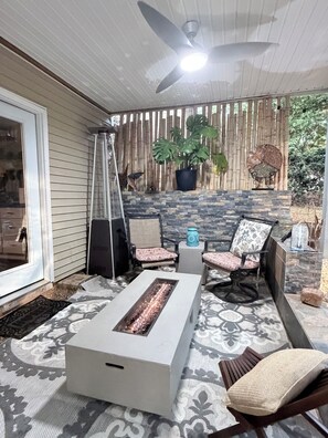 Eine Terrasse mit Feuerstelle, Sitzgelegenheiten, einem Ventilator und einem Blumentopf.