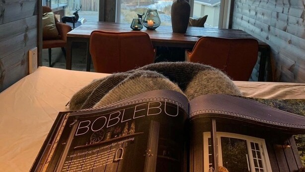 Una habitación acogedora con una cama, una mesa con un florero y velas, una ventana con vistas a montañas y una lámpara esférica única.