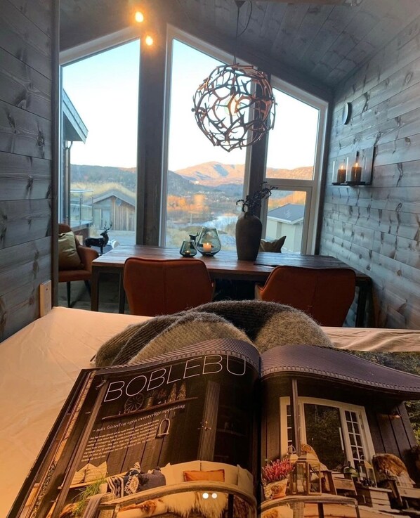 A cozy room with a bed, a table with a vase and candles, a window with a view of mountains, and a unique spherical light fixture.