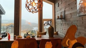 Una habitación acogedora con paredes de madera, ventanas amplias, una mesa de comedor con sillas y una lámpara colgante.
