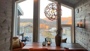 Interior de madera con una mesa, sillas, una lámpara colgante y un ventanal con vistas.