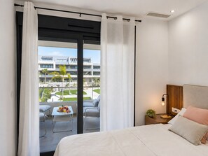 Ein Hotelzimmer mit einem Bett, einem Nachttisch mit Lampe sowie Blick auf ein modernes Gebäude und eine Außenbereichs-Sitzgelegenheit.