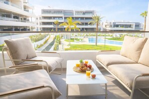 Ein Balkon mit einem weißen Tisch, zwei beigefarbenen Sofas und Blick auf ein Schwimmbad und Gebäude.