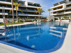 Ein Schwimmbecken mit Fliesenrand, umgeben von einem modernen Gebäude mit Balkonen und Palmen.