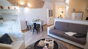 A living room with a sofa, a coffee table with a candle, and a dining area with chairs and a table. - Colleoni 20. Superior Apartment. A stylish apartment for 4 people. Upper Town (Bergamo)