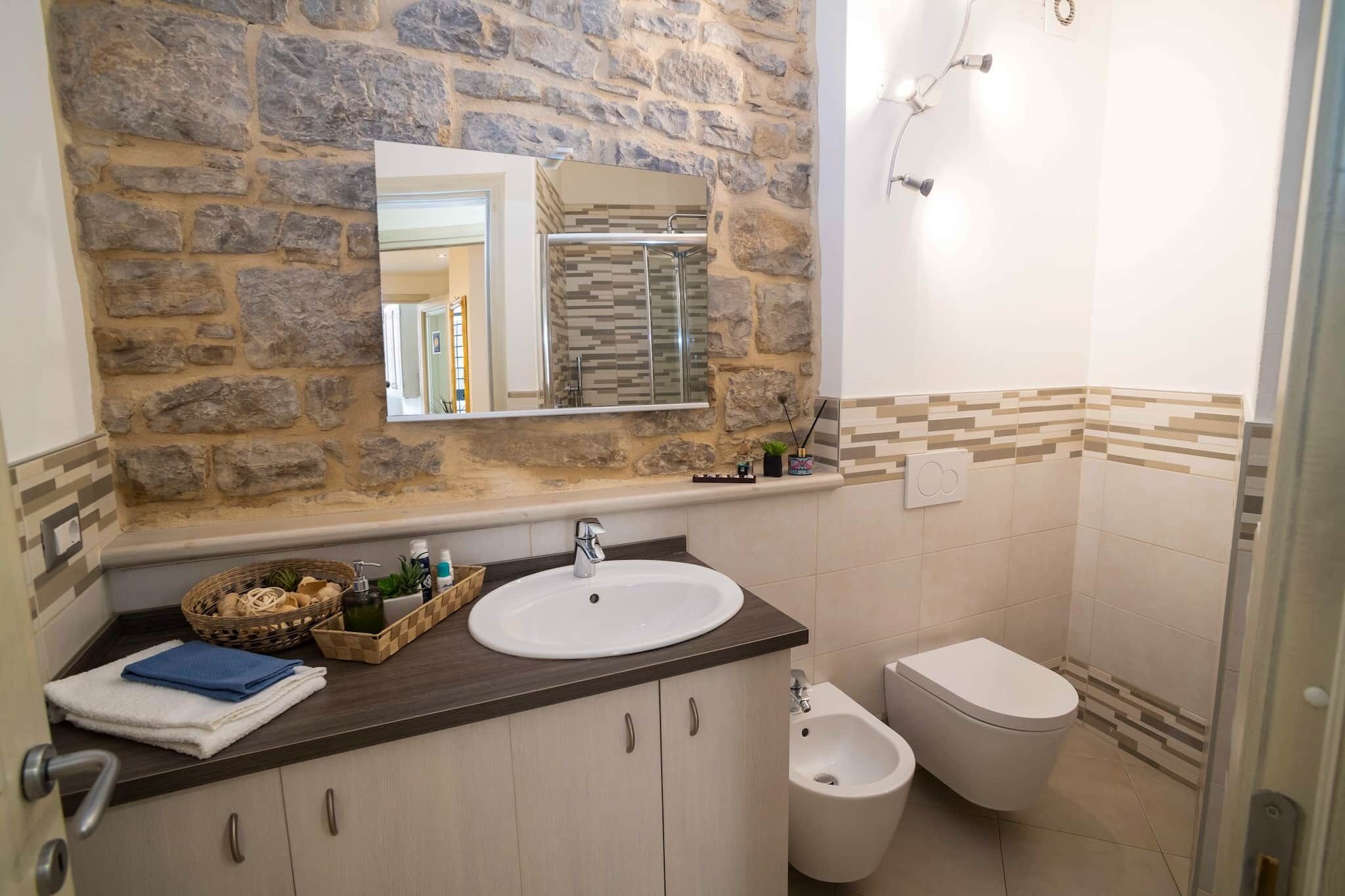 A bathroom with a stone wall, a sink, a bidet, and a mirror.