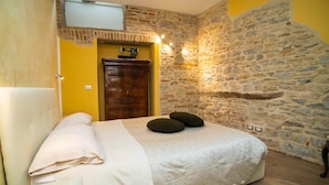 A bedroom with a bed, a wooden dresser, a stone wall, and a door. - Colleoni 20. Superior Apartment. A stylish apartment for 4 people. Upper Town (Bergamo)