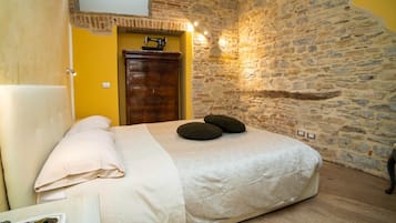 A bedroom with a bed, a wooden dresser, a stone wall, and a door.