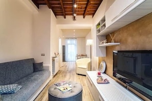 Un soggiorno con divano, poggiapiedi, televisore e un'area pranzo sullo sfondo.