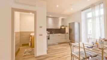 A modern kitchen with a built-in oven, a dining table with chairs, and a large window with curtains.