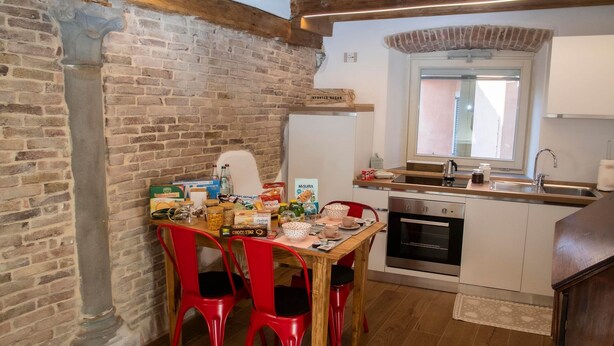 A compact kitchen with a wooden ceiling, a brick wall, a dining area with red chairs, and a small table. - The Key to Bergamo.  Il Capitello is a stylish apartment located at 112 Via Pignolo (Bergamo)