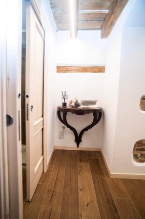 A narrow hallway with wooden flooring, a white door, and a small table with a shelf above it. - The Key to Bergamo.  Il Capitello is a stylish apartment located at 112 Via Pignolo (Bergamo)