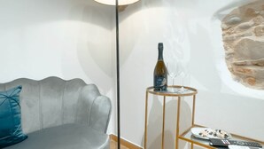 Un salon moderne avec un canapé gris, une lampe sur pied, une petite table sur laquelle se trouvent une bouteille et un verre, et un mur dont la texture rappelle celle de la pierre.