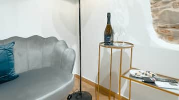Un salon moderne avec un canapé gris, une lampe sur pied, une petite table sur laquelle se trouvent une bouteille et un verre, et un mur dont la texture rappelle celle de la pierre.
