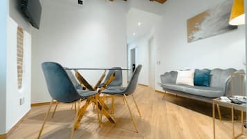 Un salon moderne comprenant un coin repas, un canapé gris et un téléviseur fixé au mur.