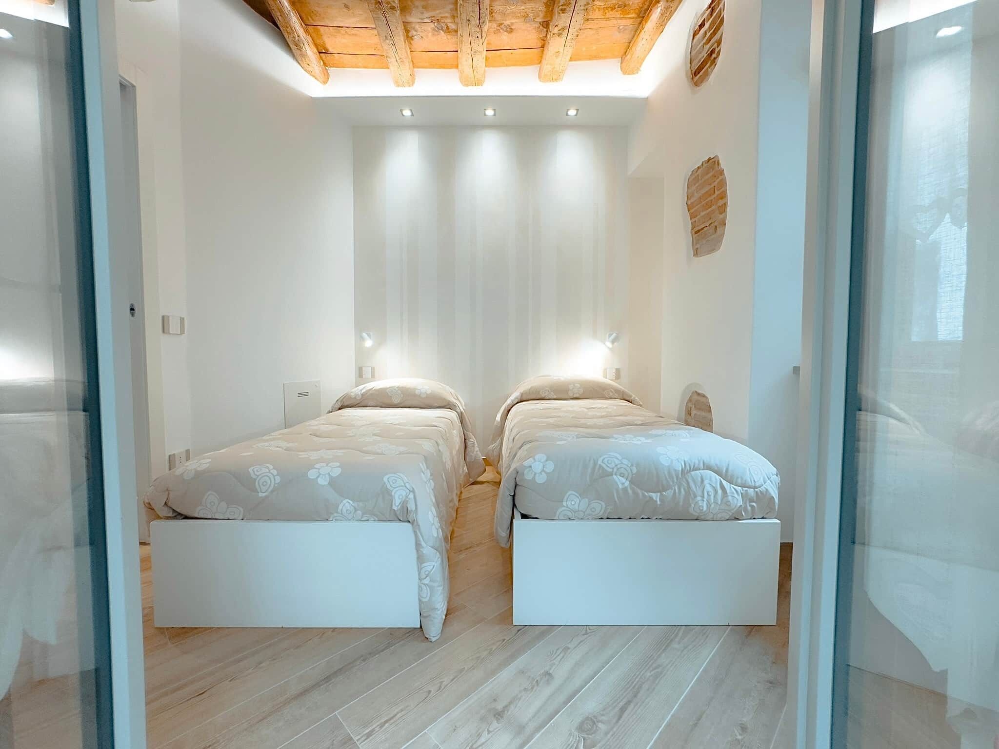 Un dormitorio con dos camas, vigas de madera en el techo y una pared blanca con un respiradero.