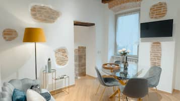 Un salon moderne comprenant un canapé, une table à manger et des chaises, une lampe et un téléviseur fixé au mur.