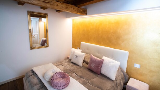A bedroom with a bed, a bedside table, a mirror, and a wall-mounted light. - The Key Of Bergamo.Fronte Mura is an elegant apartment located on Via Pignolo (Bergamo)