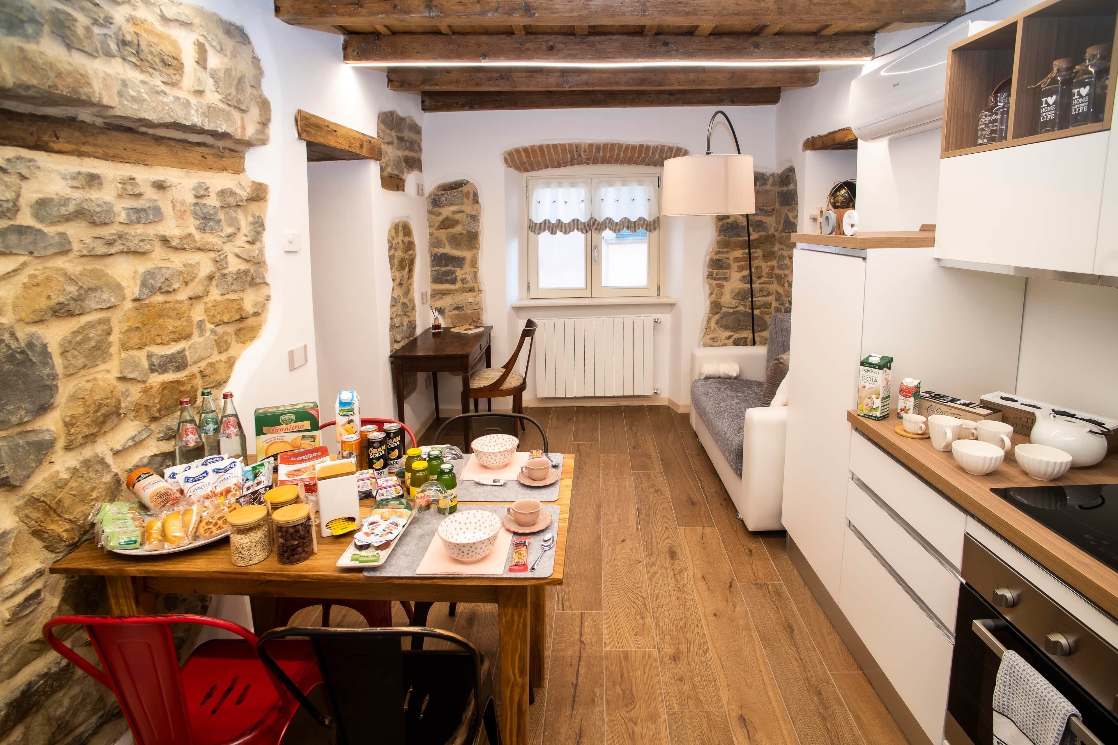 A cozy kitchen with stone walls, wooden beams, a dining area with a table set for two, and a built-in oven.