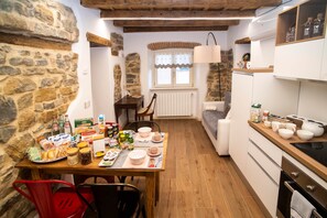 Eine gemütliche Küche mit Steinwänden, Holzbalken, einer Essecke mit Tisch für zwei Personen und einem eingebauten Backofen.