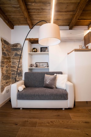 Ein gemütliches Wohnzimmer mit grauem Sofa, einer weißen Lampe und einer Steinwand.