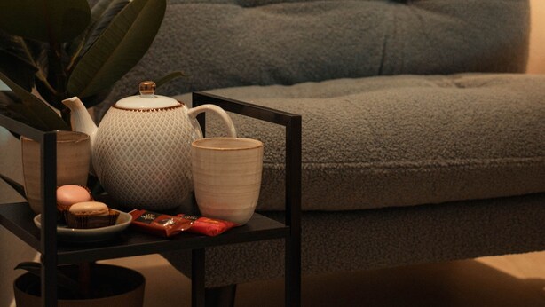 En mysig sittgrupp med en grå soffa, ett sidobord med en tekanna, en kopp och en krukväxt.