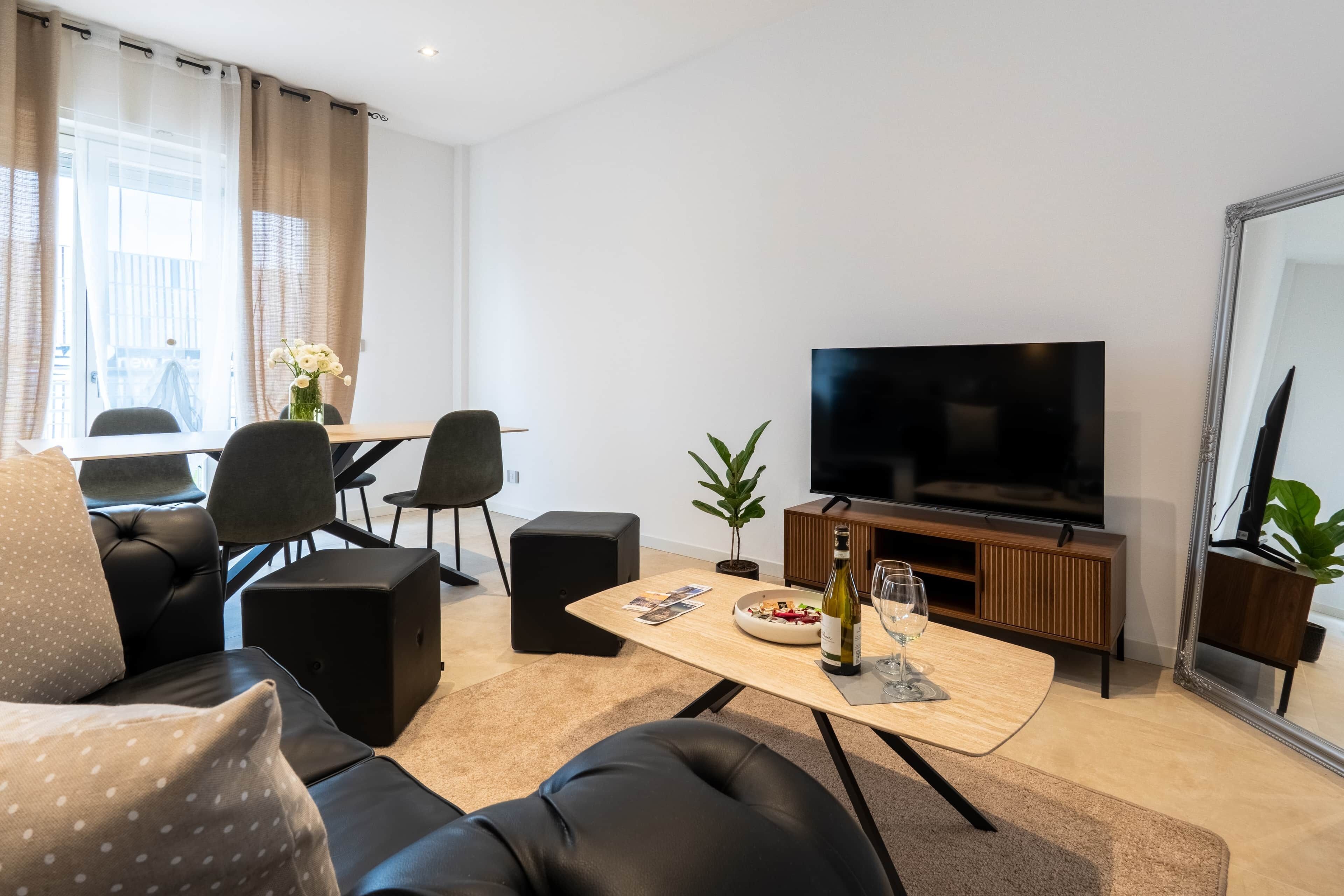 Un salon moderne comprenant un canapé, une table basse, un téléviseur et un coin repas avec des chaises et une table.