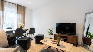 Ett modernt vardagsrum med en soffa, ett soffbord, en tv och en matplats med stolar och ett bord.