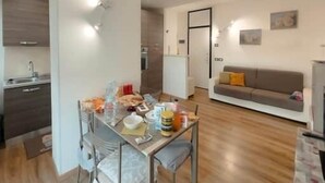 Een moderne woonkamer met een bank, een eettafel met stoelen en een keuken op de achtergrond.