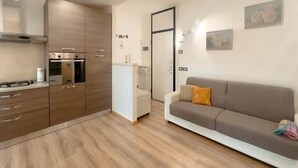 Een moderne keuken met inbouwapparatuur, een eethoek met een witte tafel, en een woonkamer met een bank en een deur naar een andere kamer.
