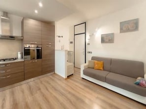 A modern kitchen with built-in appliances, a dining area with a white table, and a living room with a sofa and a door leading to another room. - Carrara Hospital Home. A bright and modern apartment located at Via delle Cave 9 (Bergamo)