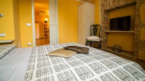 Ein Schlafzimmer mit einem gemusterten Bettbezug, einem an einer Steinwand montierten Fernseher und einem Kleiderschrank.