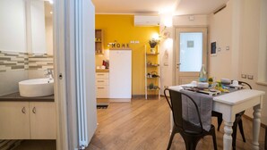 Eine Küche mit weißem Spülbecken, einem Esstisch mit Stühlen, einem Kühlschrank und einer gelben Wand.