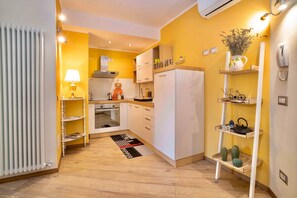 A compact kitchen with white cabinets, a stove, and a refrigerator. There are shelves with decorative items and a small plant. - Colleoni 20. Standard Apartment. Apartment located in the Upper Town, at Via Colleoni 20. (Bergamo)