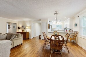 A spacious living room with a dining area, wooden flooring, and a kitchen in the background. - Grace Haven (Lake Junaluska)
