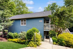 A two-story blue house with a balcony, number 155, surrounded by greenery. - Grace Haven (Lake Junaluska)