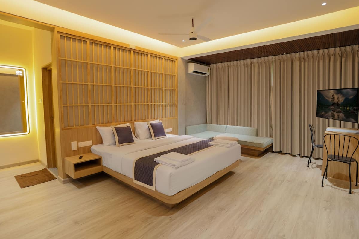 Una habitación de hotel moderna con una cama grande, una zona de estar, un escritorio y un ventanal con cortinas.