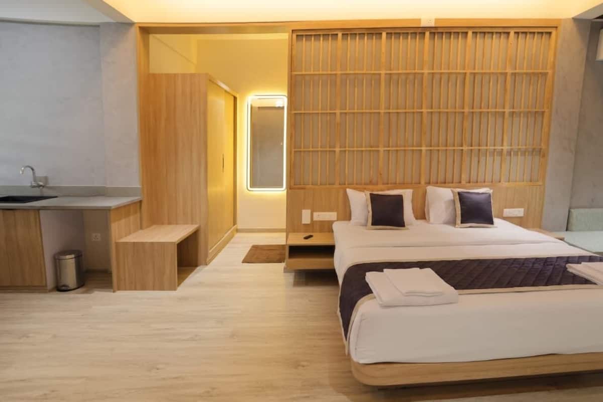 Una habitación de hotel moderna con una cama de madera, una mesita de noche, un escritorio pequeño con lavamanos y un vestidor.