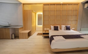Een moderne hotelkamer met een houten bed, een nachtkastje, een klein bureau met een wastafel en een inloopkast.