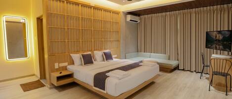 A modern hotel room with a large bed, a seating area, a desk, and a large window with curtains.