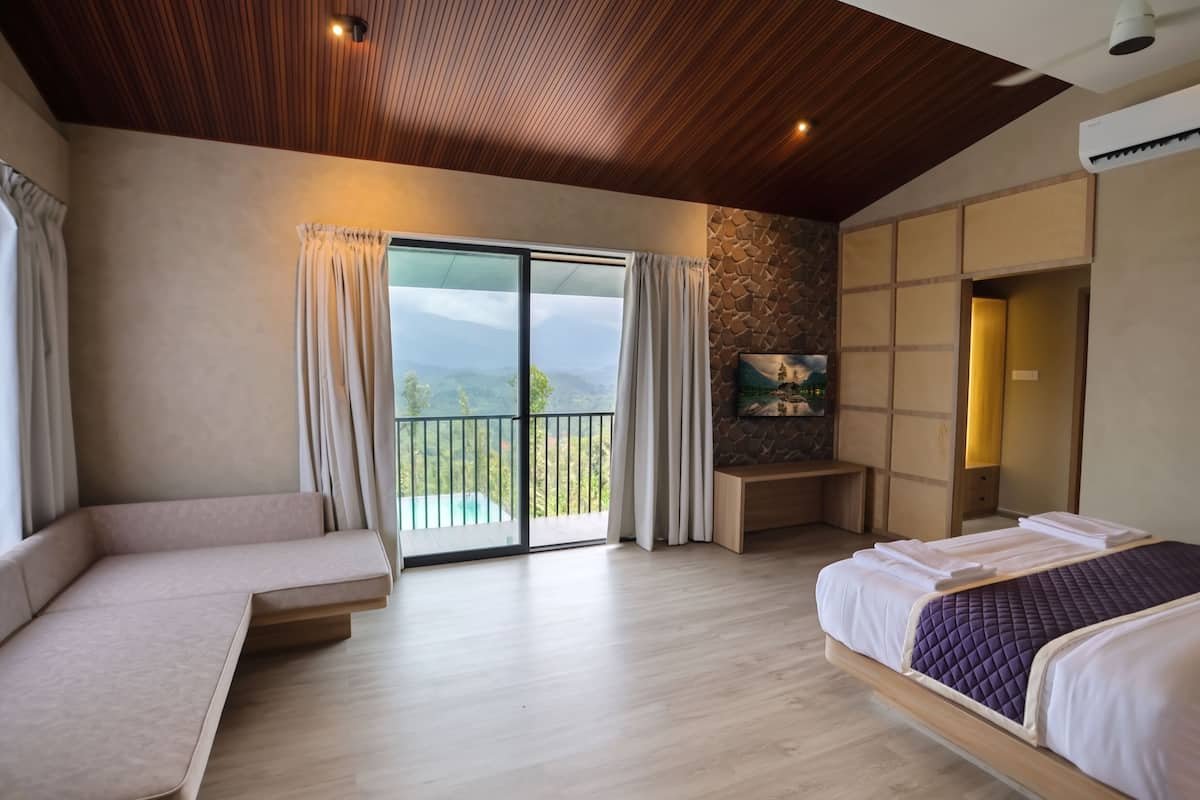 Un dormitorio con sofá, cama, televisión, pared de piedra y balcón con vistas.