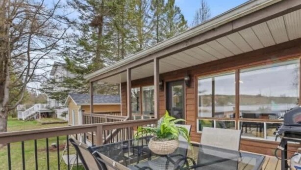 A covered deck with a glass table and chairs, a potted plant, and a view of a lake. - Waterfront & Spa | Le Petit Georges (Saint-Georges-de-Windsor)