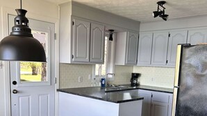 A kitchen with white cabinets, a wooden dining table, and a black refrigerator. - Waterfront & Spa | Le Petit Georges (Saint-Georges-de-Windsor)