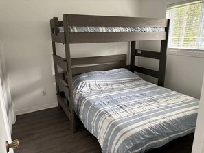 Una cama litera con colcha a rayas, una ventana con persianas y una puerta con picaporte de latón.