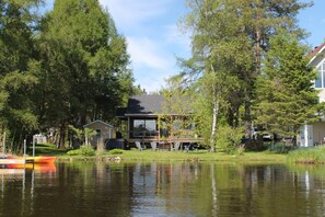 A lakeside cabin with a deck, surrounded by trees and a dock with boats.