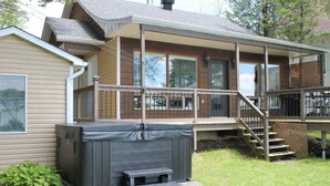 A two-story house with a deck, a hot tub, and a staircase leading to the upper level. - Waterfront & Spa | Le Petit Georges (Saint-Georges-de-Windsor)